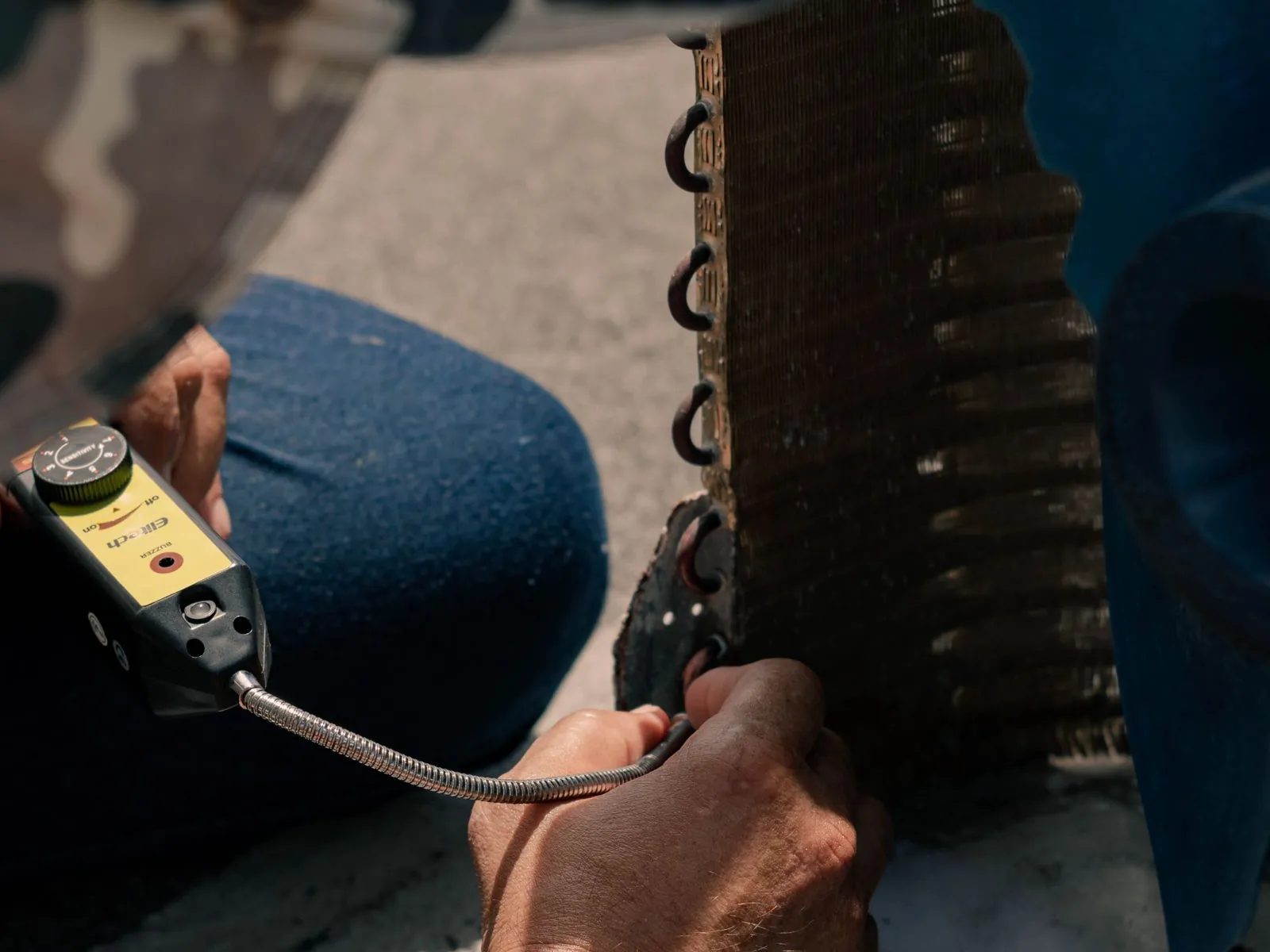 Technician performing a seasonal tune-up with a refrigerant leak detector on an outdoor coil